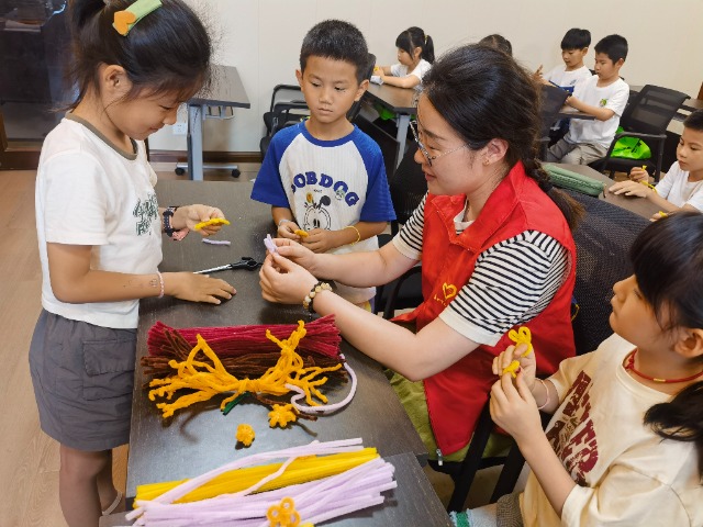 7月12日，在泰州市海陵区城东街道林湖社区，泰州市大浦小学“绿叶”暑期公益班的老师正在教孩子们一起做手工2（拍摄者：泰州市大浦中心小学  陈惠婷）.jpg